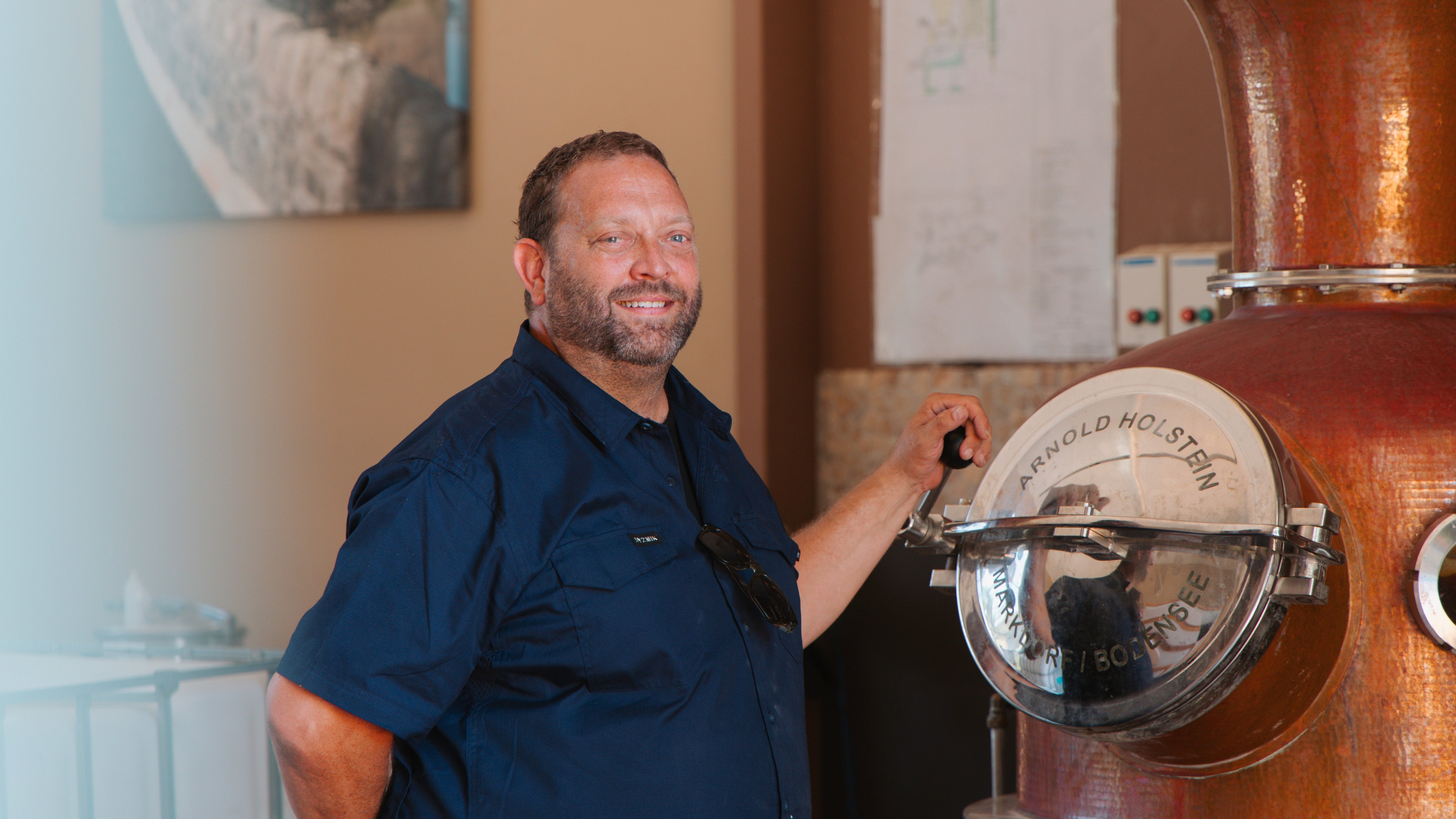 Man operating a large copper still in a distillery setting